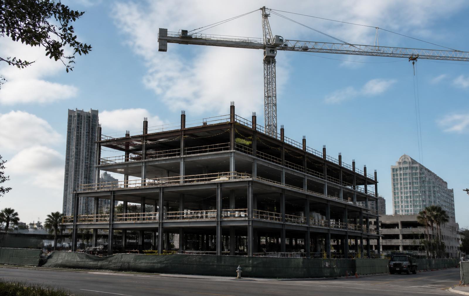 Mid-rise commercial building shell under construction with a tower crane overhead